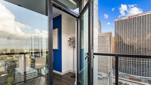 A modern hotel room with a large glass door, a blue accent wall, a potted plant, and a view of the Marriott Marquis building.
