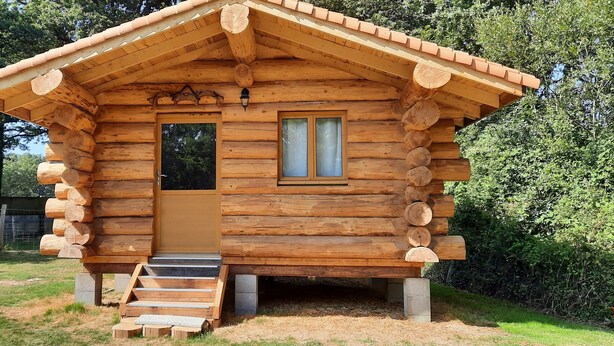 Una cabaña de madera con una puerta principal, una ventana y unos escalones de madera que conducen a la entrada.