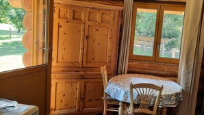 Interior de una cabaña de madera con una mesa de comedor y sillas, una ventana que ofrece vistas a la vegetación y armarios de madera.