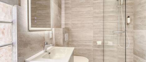 A modern bathroom with a glass shower enclosure, a white sink, and a toilet.