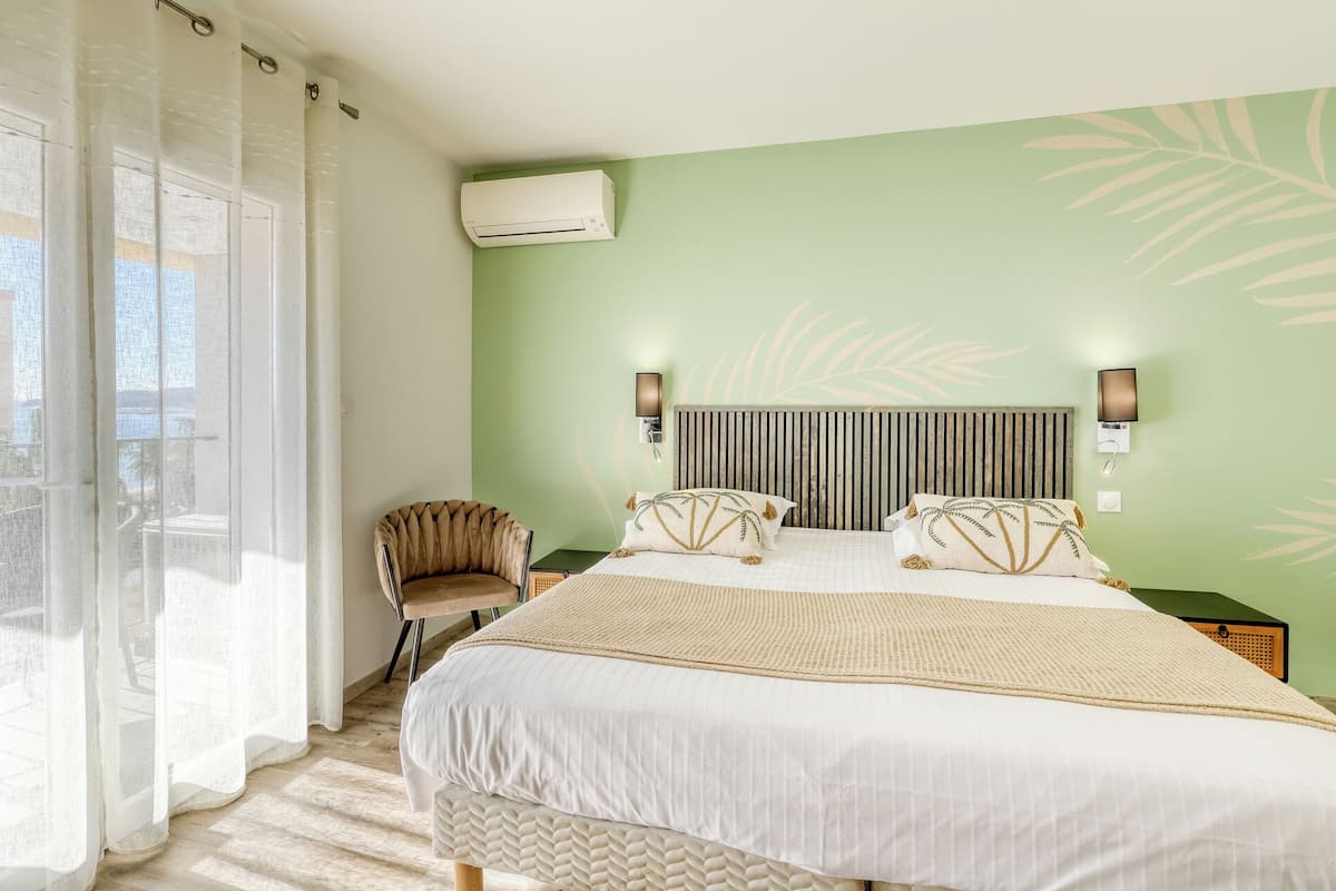 A bedroom with a bed, a chair, an air conditioning unit, and a view of the outdoors.