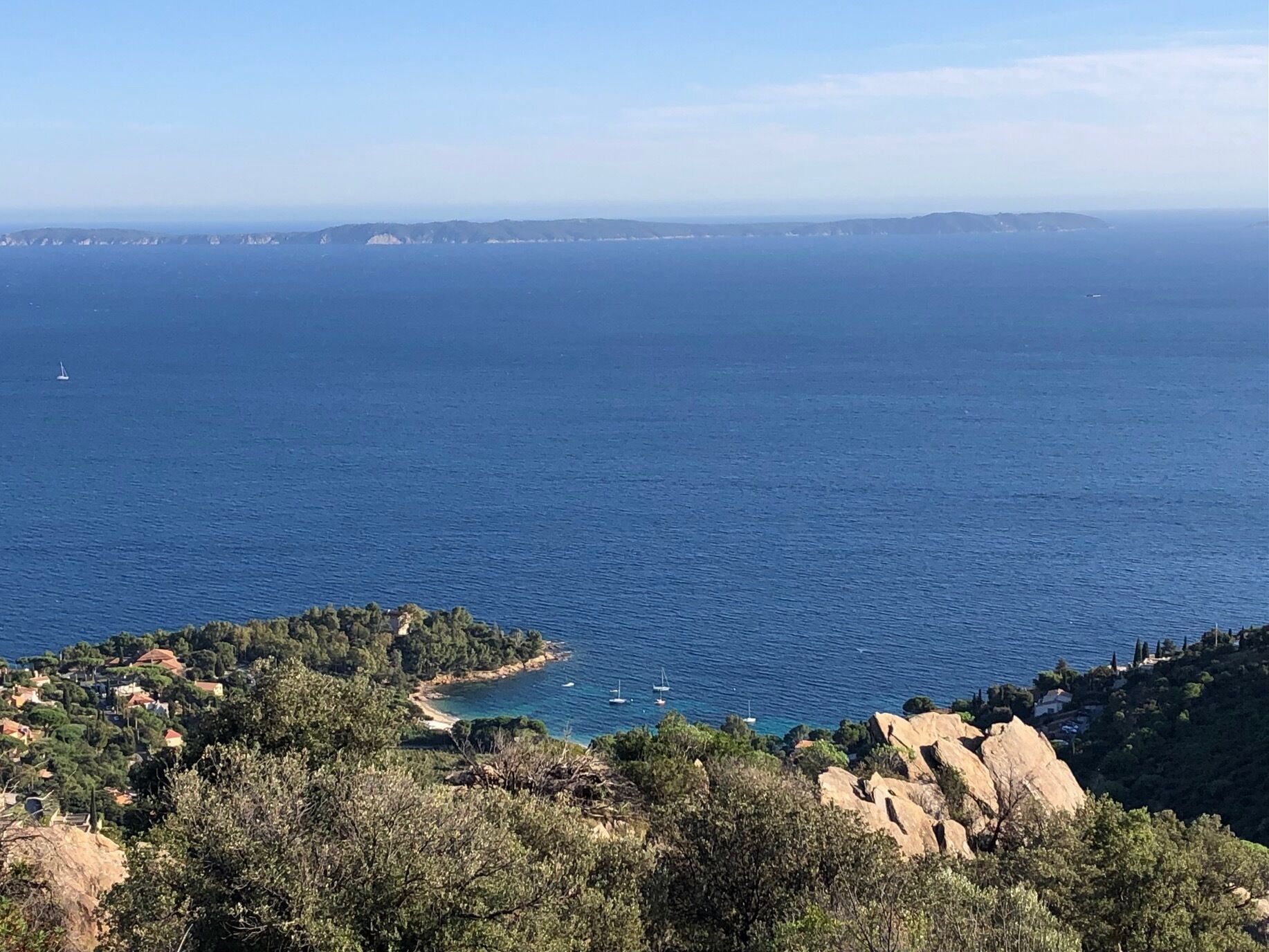 A coastal landscape with a clear view of the sea, rocky terrain, and a small settlement with houses.