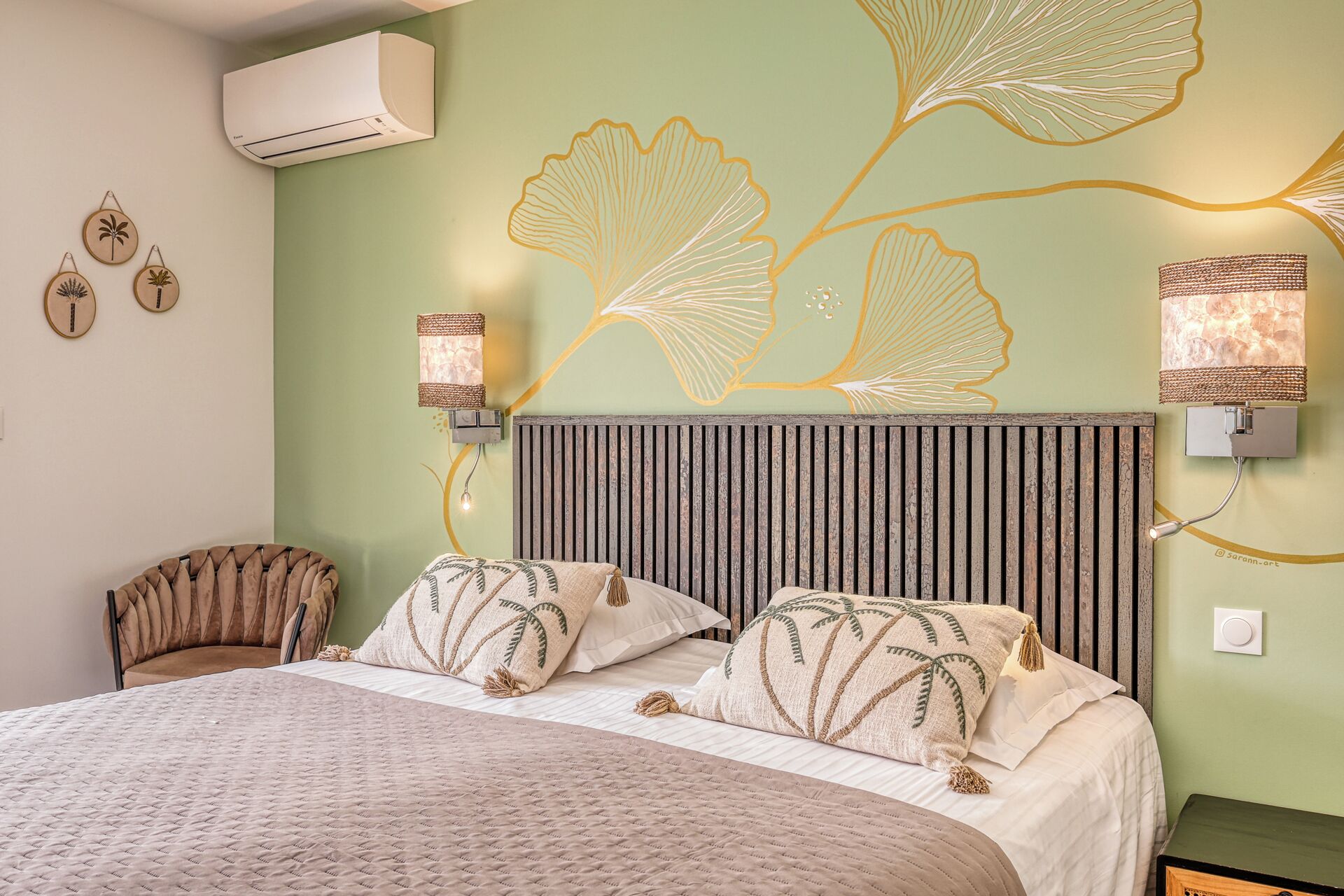 A bedroom with a bed, a wall-mounted air conditioner, decorative wall art, and a bedside lamp.