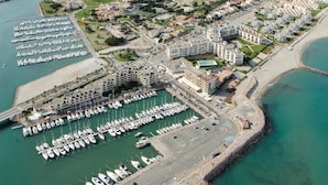 An aerial view of a marina with numerous boats docked, surrounded by residential buildings and a beach.