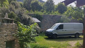 A stone wall, a white van, and a stone structure with a flat top.