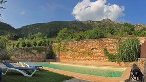 A swimming pool with stone walls and a grassy area with lounge chairs.