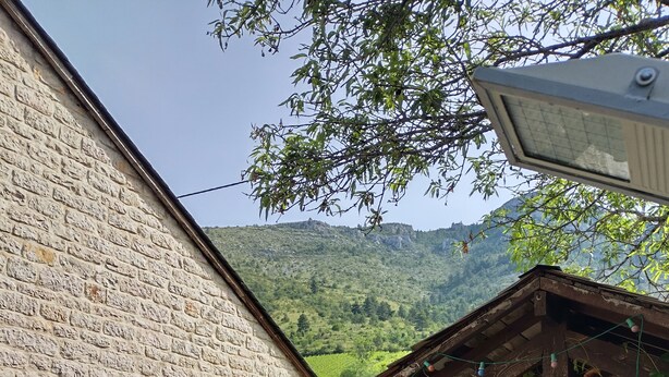 A stone building with a wooden porch, a stone fireplace, and a view of green hills.