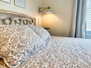 Une chambre à coucher avec un lit, une lampe fixée au mur et une fenêtre avec des rideaux.