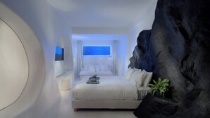 A modern bedroom with a bed, a seating area, and a large rock feature. - Million Stars Mykonos (Mykonos)