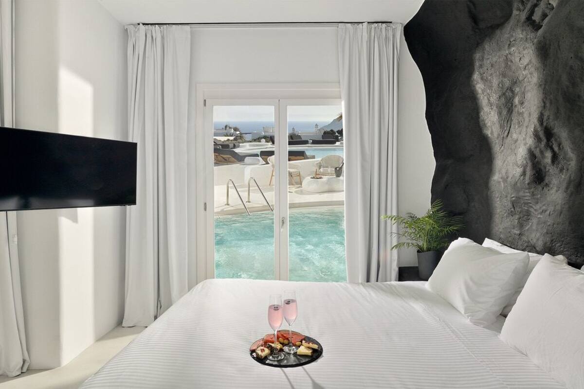 A hotel room with a bed, a TV, a balcony with a pool, and a view of the ocean.
