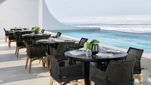 An outdoor dining area with round tables and wicker chairs, overlooking a clear blue ocean. - Million Stars Mykonos (Mykonos)