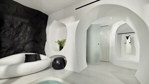 A modern spa room with a black textured wall, a white curved bench, a small black vase with a plant, and a white bathtub. - Million Stars Mykonos (Mykonos)