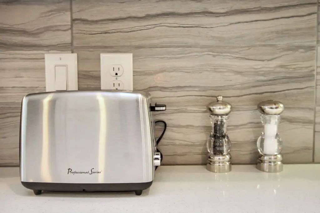 A kitchen with a stainless steel toaster on a countertop, a wall socket, and two salt and pepper shakers.