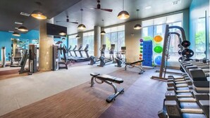 Ein Fitnessstudio mit Trainingsgeräten, großen Fenstern und einem Deckenventilator.