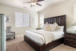 Quarto com uma cama grande, um ventilador de teto e uma cadeira.