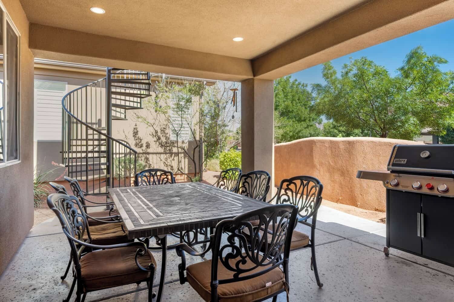 Une terrasse extérieure avec une table et des chaises, un barbecue et un escalier en colimaçon menant à un niveau supérieur.