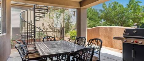 Une terrasse extérieure avec une table et des chaises, un barbecue et un escalier en colimaçon menant à un niveau supérieur.