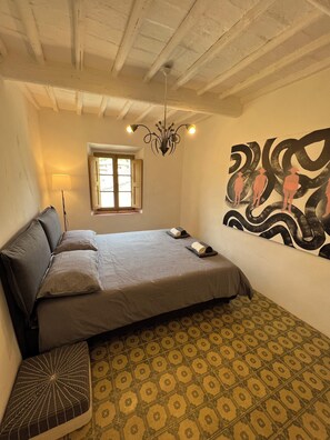 Quarto com cama, janela, lustre e pintura na parede.