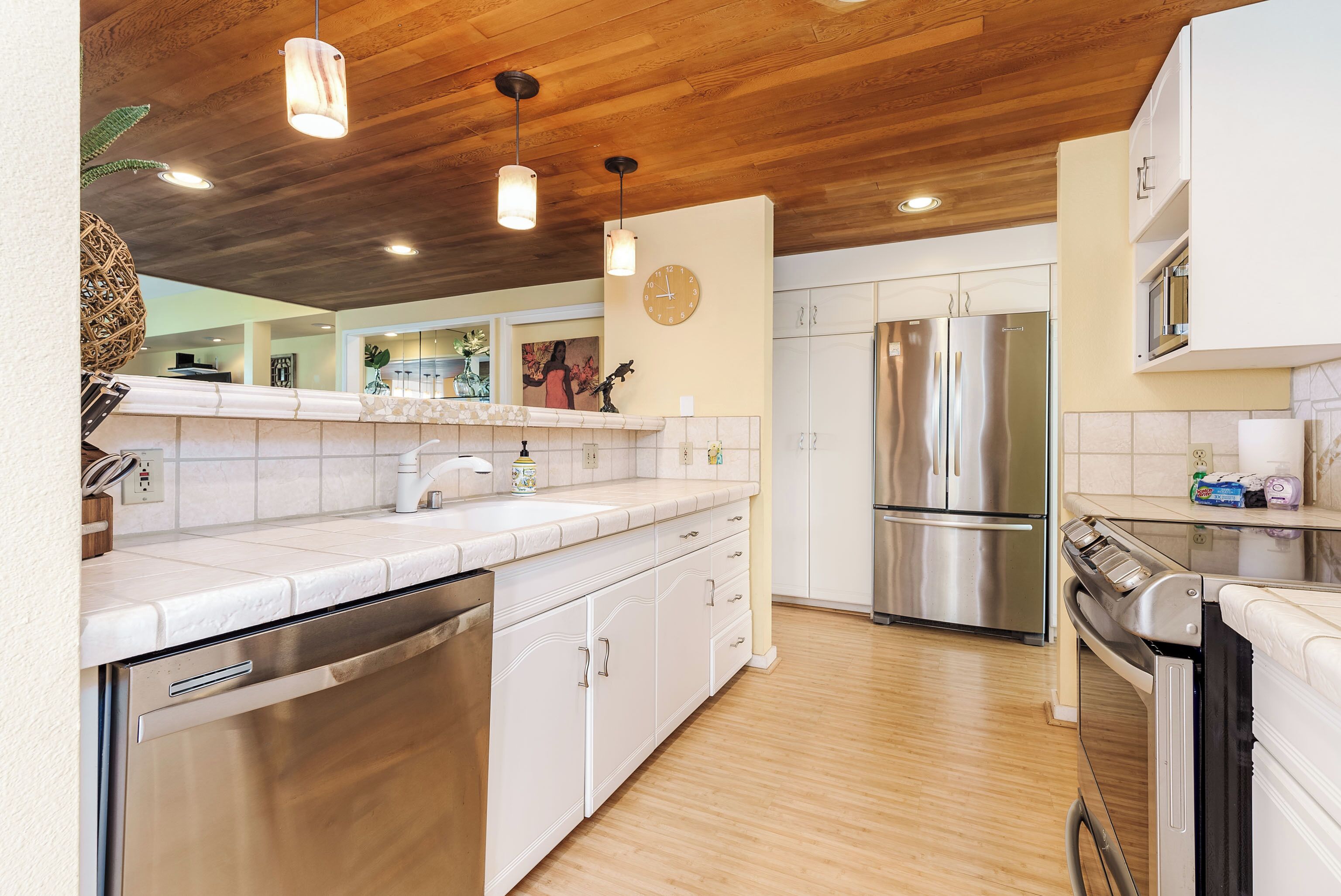 Una cocina moderna con armarios blancos, electrodomésticos de acero inoxidable y detalles de techo de madera.