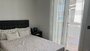 Un dormitorio con una cama, una mesita de noche, un ventilador y una ventana con cortinas.