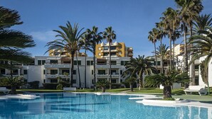 Una piscina rodeada de palmeras y un edificio de hotel con varios balcones.