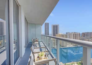 A balcony with a glass railing, a table with chairs, and a view of a cityscape with high-rise buildings.