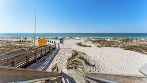 Ein Strand mit einer hölzernen Prominade, die zum Wasser führt, Sanddünen und Sonnenschirmen am Ufer.