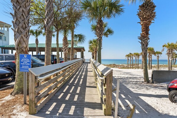 Walk along the boardwalk to the beach, flanked by tall palm trees.