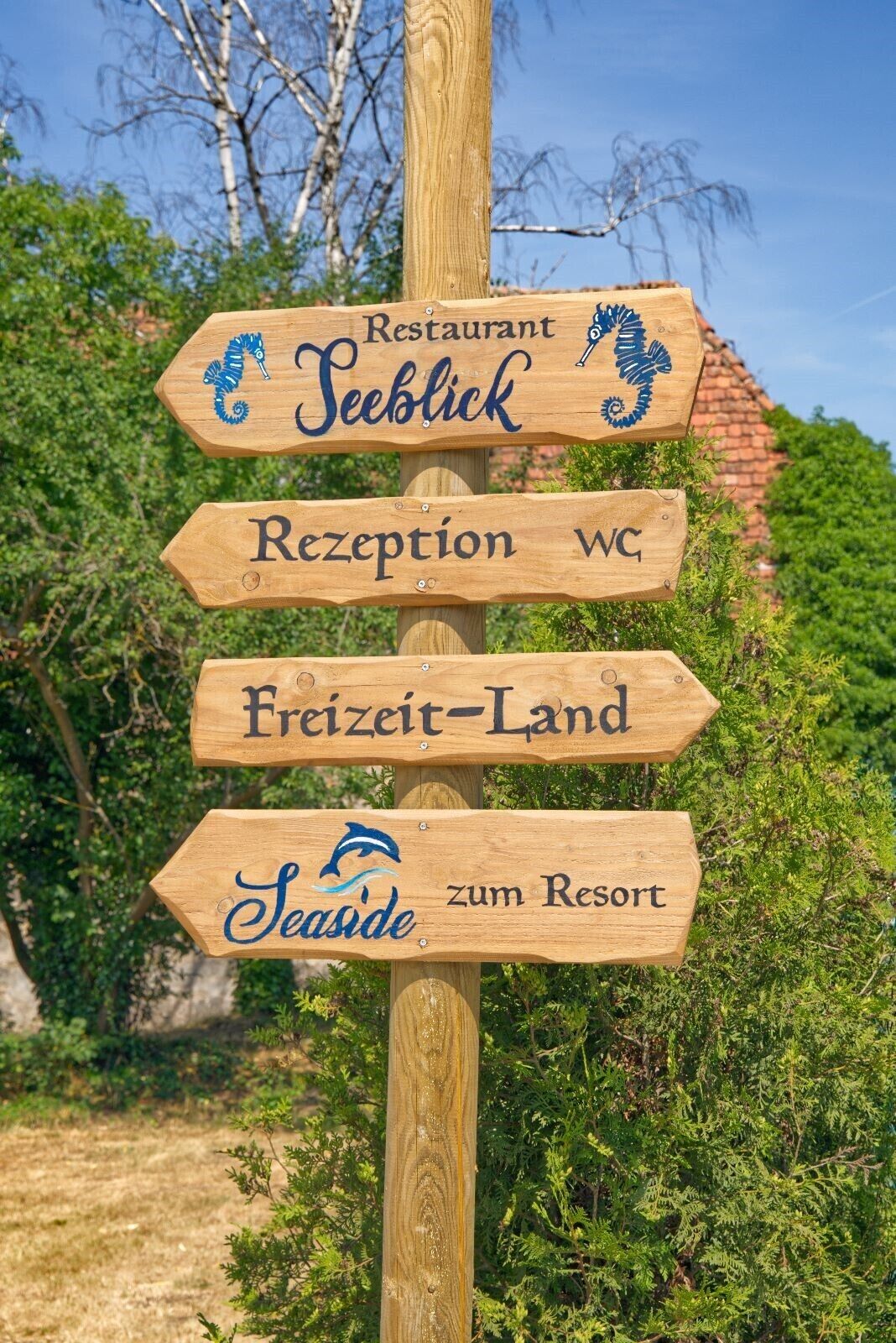 Ein hölzernes Wegweiser mit Schildern, die einen Restaurant, die Rezeption, ein Freizeitgelände und ein Resort anzeigen.