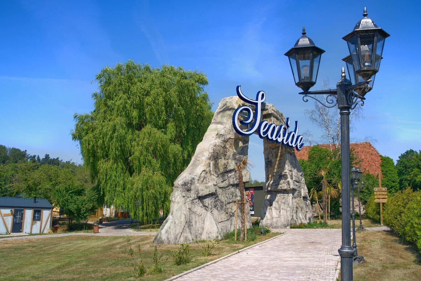 A pathway leading to a sign that reads "Seaside" with a large rock formation and a street lamp.