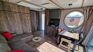 A modern living room with a sofa, a small round table, and a dining area with a wooden table and chairs. - Seaside-Resort (Geiselwind)