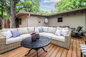 Un área de estar techada al aire libre con un sofá modular, una mesa redonda y una pérgola.