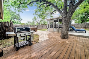 A backyard with a grill, a covered patio, and a wooden deck.