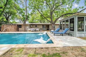 A backyard with a swimming pool, lounge chairs, and a covered patio area.