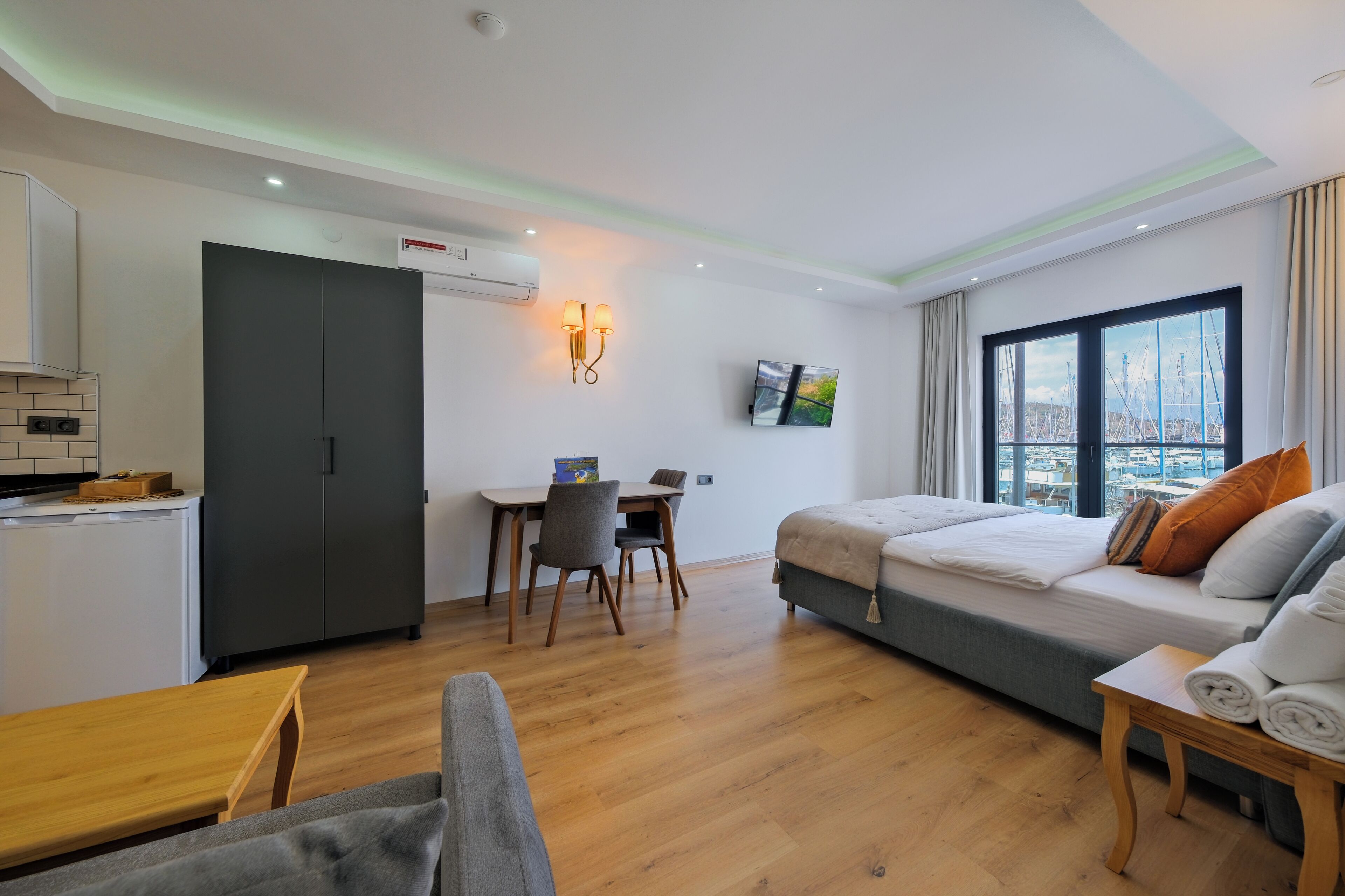 A compact hotel room with a kitchenette, a dining area, a bed with pillows, and a window with a view.