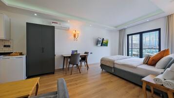 A compact hotel room with a kitchenette, a dining area, a bed with pillows, and a window with a view.