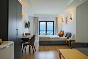 Een moderne hotelkamer met een bed, een bureau, een stoel, een bank en uitzicht op zee.