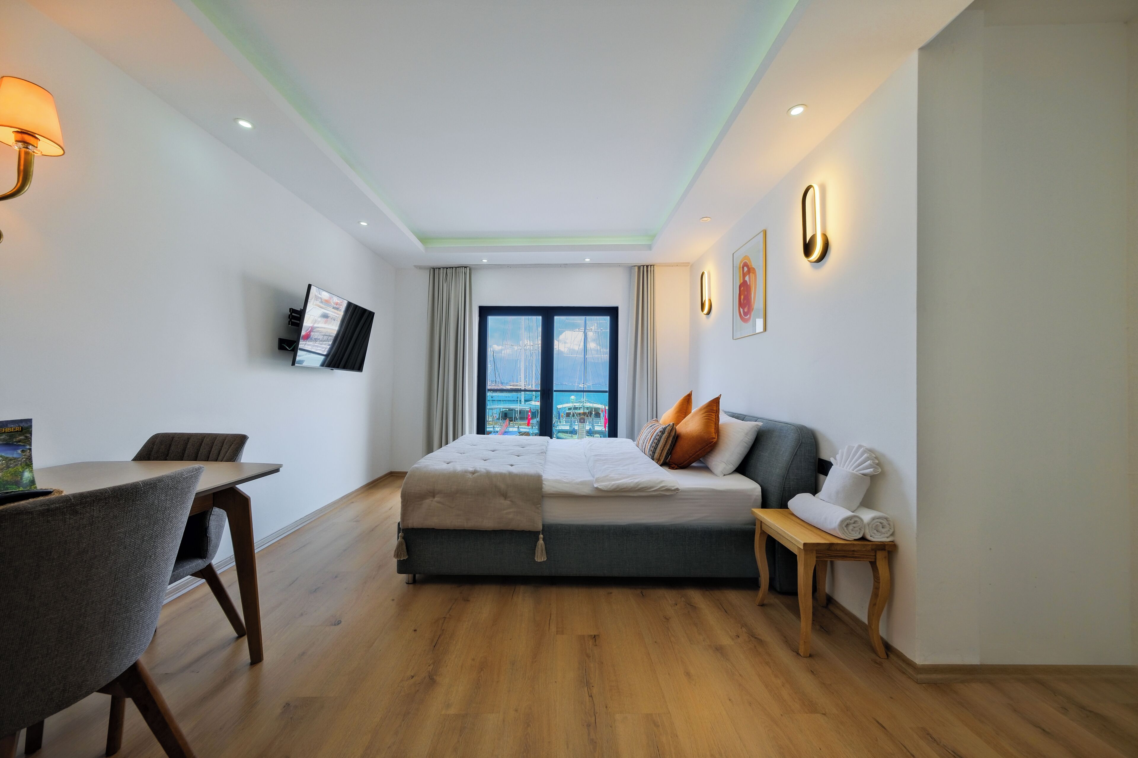 Habitación de hotel moderna con cama, escritorio, silla, televisor y ventana con vista a la ciudad.