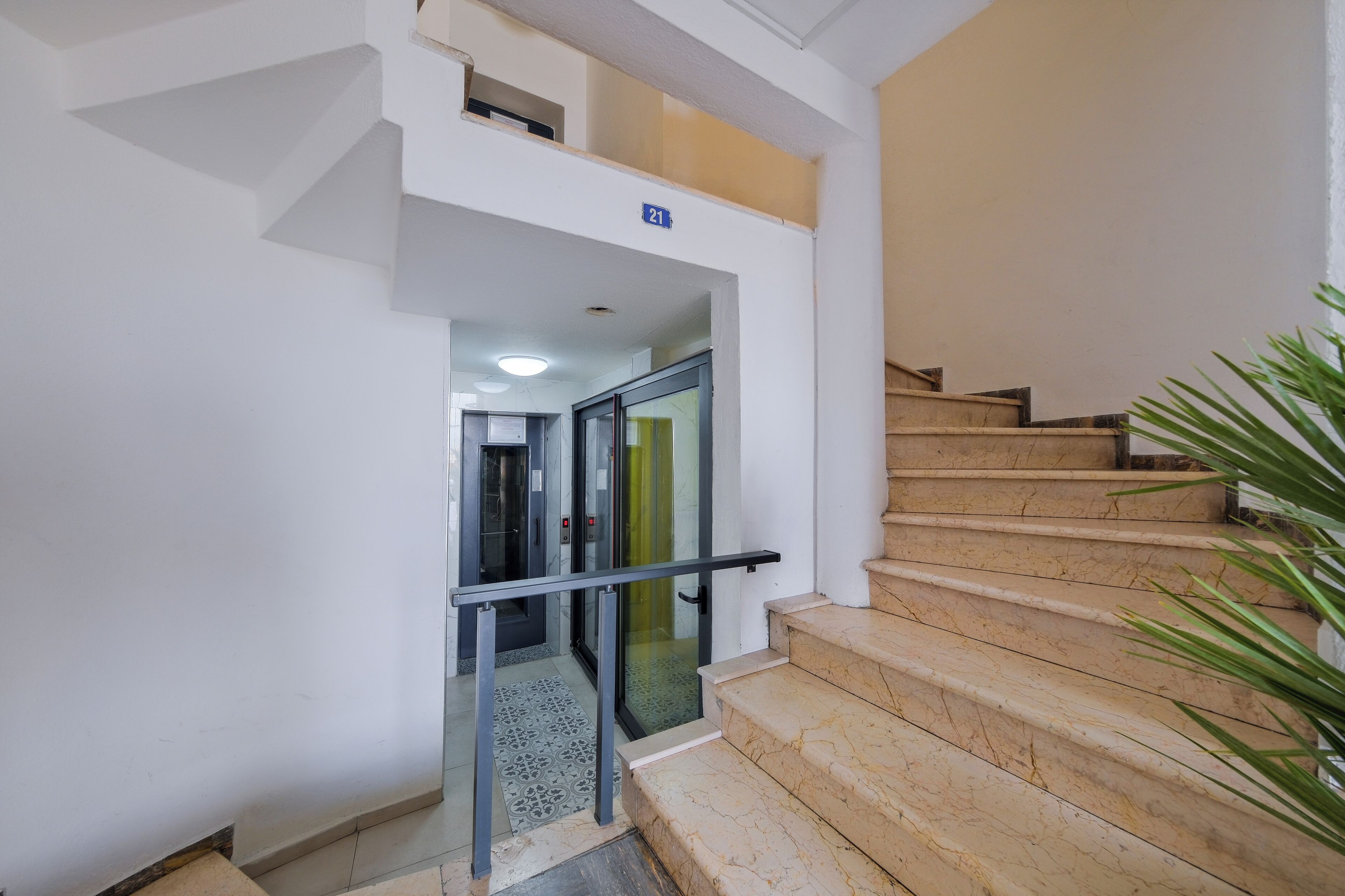Un escalier avec des marches en marbre et une porte en verre donnant sur un espace intérieur.