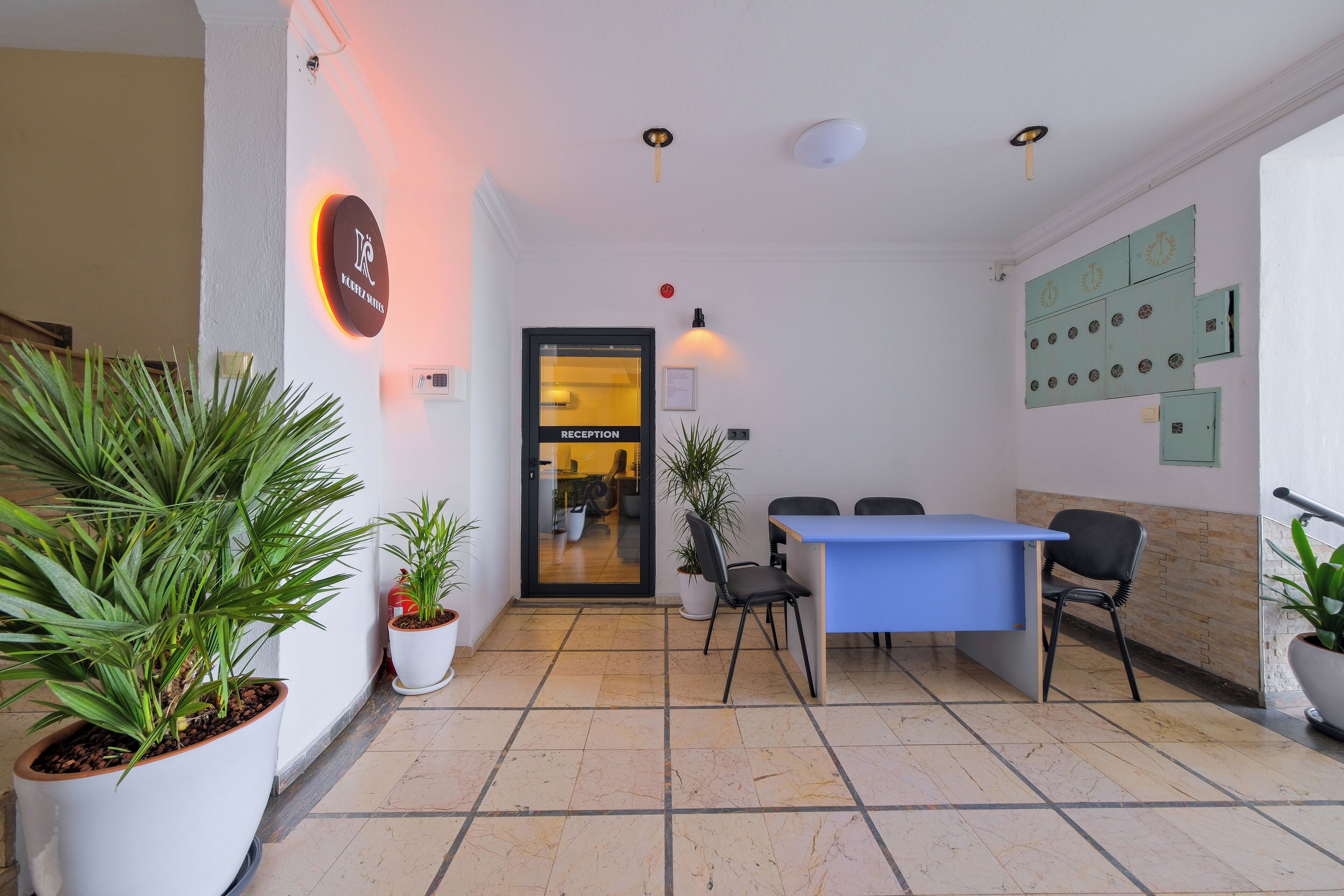A reception area with a reception desk, chairs, potted plants, and a reception sign.