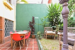 A patio area with a table and chairs, surrounded by potted plants and a green wall.