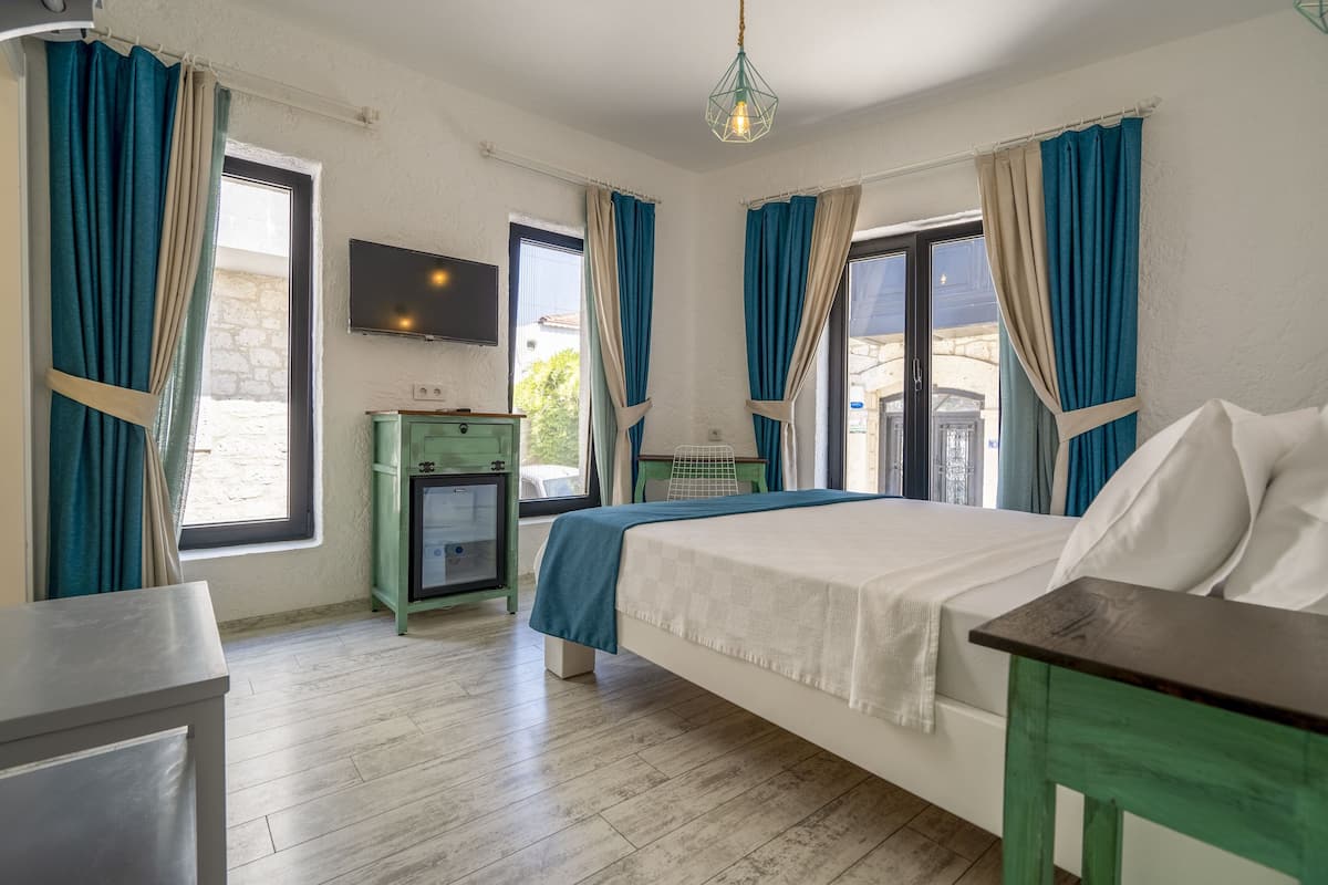 A bedroom with a bed, a TV, a desk, and a window with curtains.