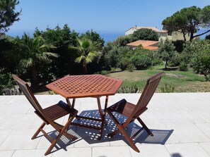 A patio with a table and two chairs, overlooking a garden and a view of the sea. - Appart , Belles Prestations Avec Terrasse vue mer Dans Villa (.CALCATOGGIO)
