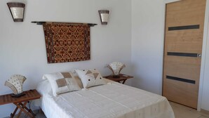 Une chambre à coucher avec un lit, deux tables de chevet, une lampe fixée au mur, une tapisserie à motifs et une porte en bois.