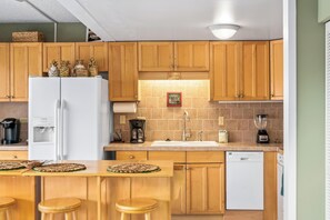 Une cuisine avec des meubles de rangement en bois, un réfrigérateur blanc, une machine à café, un mixeur et un lave-vaisselle.