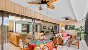 A spacious living area with a dining table, wicker furniture, and ceiling fans.