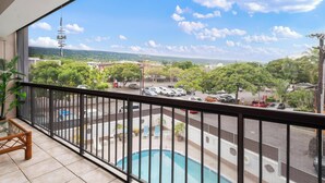 A balcony with a pool, a view of a parking lot, and a distant landscape.