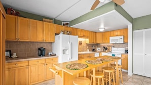 A kitchen with wooden cabinets, a white refrigerator, a microwave, and a bar area with stools.