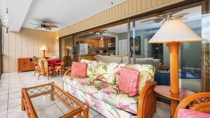 A spacious living area with a sofa, chairs, a dining table, and a ceiling fan.