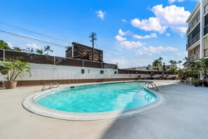 A swimming pool with a concrete deck, surrounded by potted plants and a fence.